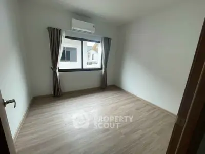 Spacious empty bedroom with large window and wooden flooring
