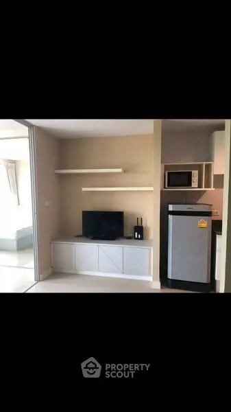 Modern living room with sleek TV unit and compact kitchen appliances.