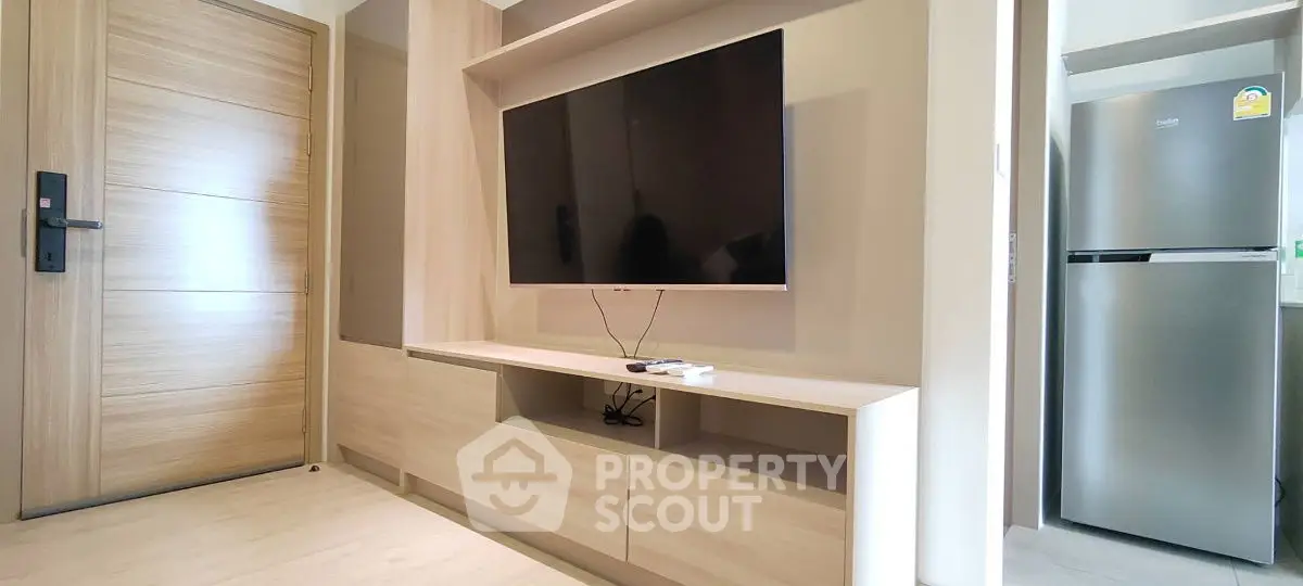 Modern living room with sleek TV setup and stainless steel fridge in open layout.