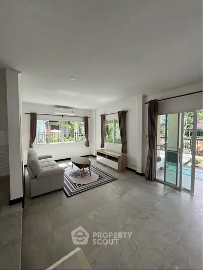 Spacious living room with modern decor and large windows offering natural light and garden view.