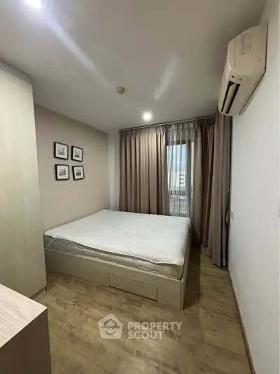 Cozy bedroom with wooden flooring, air conditioning, and natural light through large window.