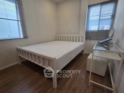 Cozy bedroom with wooden flooring and ample natural light from two windows.