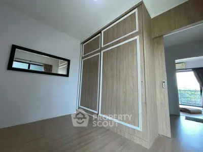 Spacious bedroom with built-in wooden wardrobe and large window view.