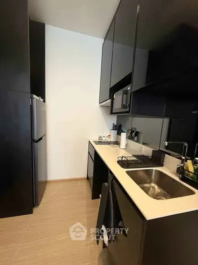 Modern kitchen with sleek black cabinets and stainless steel appliances in a compact layout.