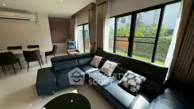 Spacious living room with modern black leather sofa and garden view, perfect for relaxation.