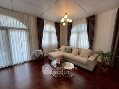 Elegant living room with modern chandelier and cozy sectional sofa, featuring large windows with sheer curtains.