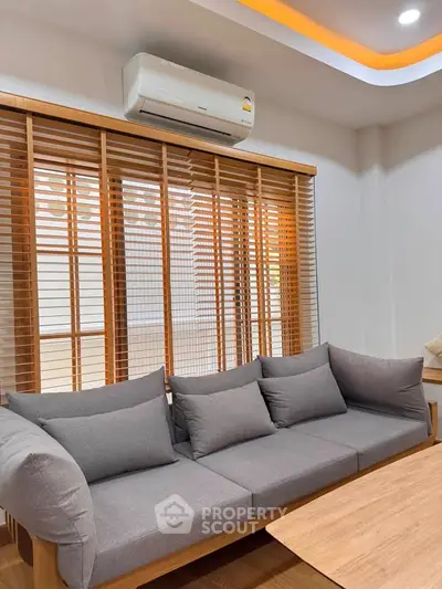 Modern living room with stylish grey sofa and wooden blinds, featuring a sleek air conditioning unit.