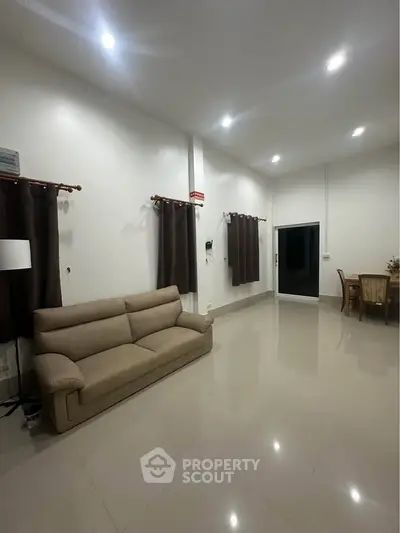 Spacious living room with modern sofa and dining area, featuring high ceilings and elegant lighting.