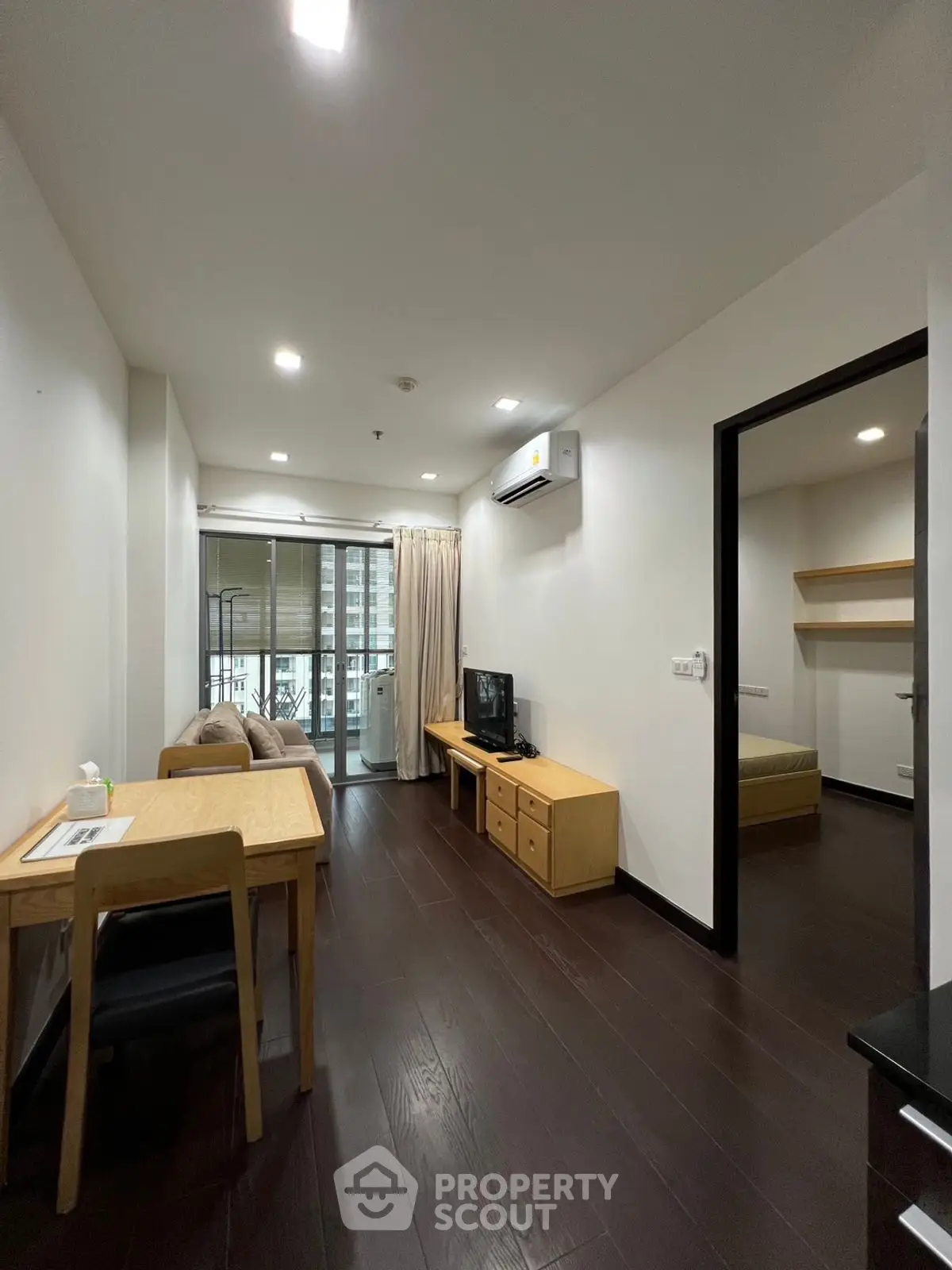 Modern apartment with open living room and balcony view, featuring sleek wooden flooring and cozy furnishings.