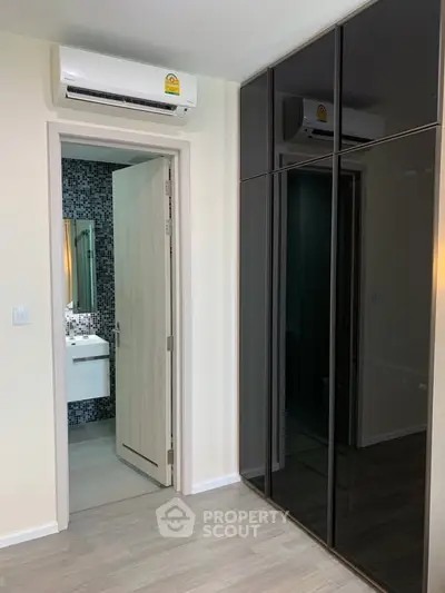 Modern bedroom with sleek black wardrobe and en-suite bathroom featuring stylish mosaic tiles.