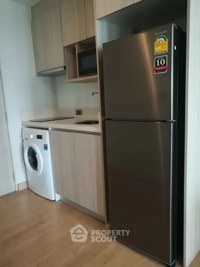 Modern kitchen with sleek appliances including fridge and washing machine in compact layout.