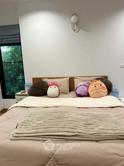 Cozy bedroom with plush pillows and natural light from large window.