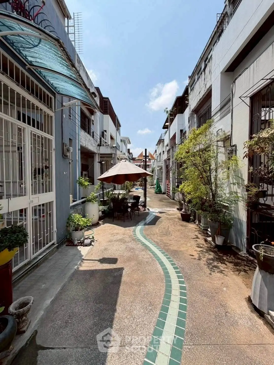 Charming residential alley with outdoor seating and lush greenery, perfect for urban living.