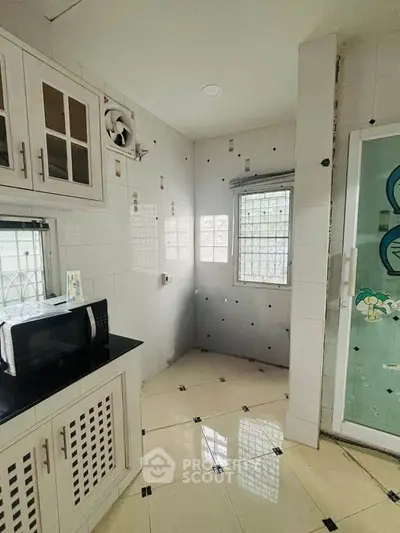 Compact kitchen with microwave and tiled walls, featuring a small window for natural light.
