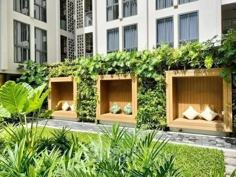 Luxurious garden area with stylish wooden seating and lush greenery in modern apartment complex.