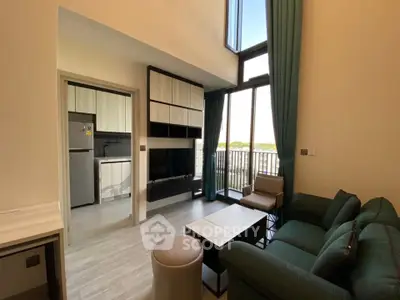 Modern living room with high ceiling and large windows, adjacent to a compact kitchen.