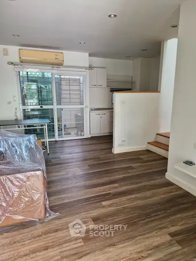 Modern living room with sleek wooden flooring and staircase, featuring a compact kitchen area.