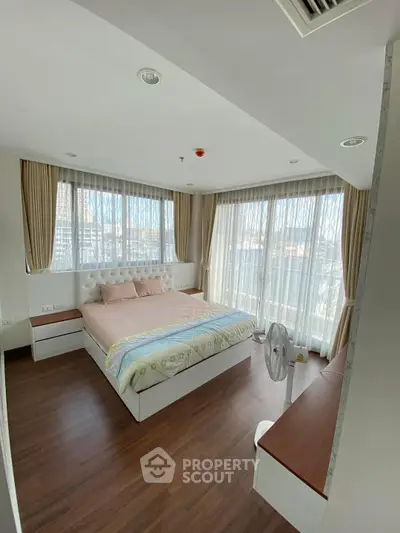 Spacious bedroom with large windows and elegant decor, offering abundant natural light and a cozy atmosphere.