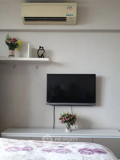 Modern bedroom with wall-mounted TV and air conditioning, featuring elegant decor and fresh flowers.