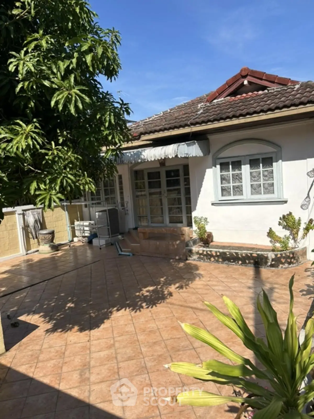 Charming single-story house with tiled patio and lush greenery, perfect for outdoor relaxation.