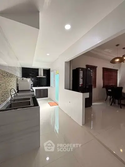 Modern kitchen with open layout and dining area, featuring sleek appliances and stylish lighting.
