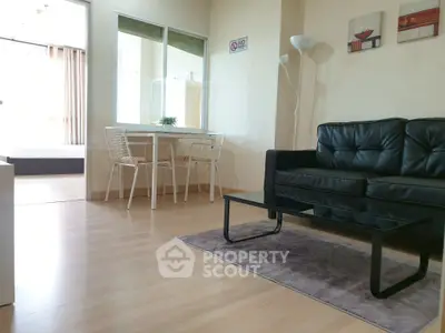 Modern living room with sleek black sofa and glass coffee table, adjacent to dining area.