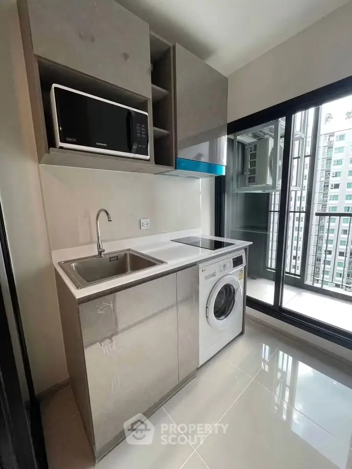 Modern compact kitchen with washing machine and microwave, featuring sleek cabinetry and balcony view.