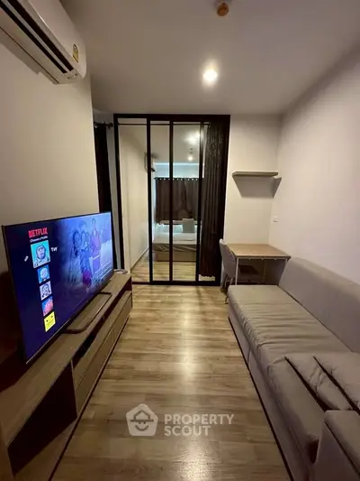 Modern living room with sleek design, featuring a cozy sofa, flat-screen TV, and stylish partition leading to bedroom.
