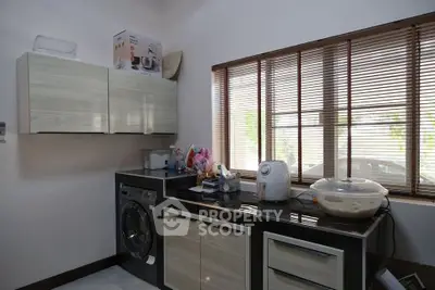Modern kitchen with sleek cabinets and washing machine, ample natural light from large window.