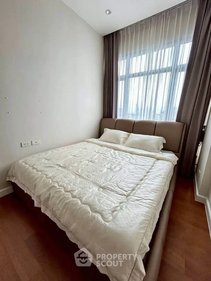 Cozy bedroom with large window and elegant curtains, featuring a comfortable bed and wooden flooring.