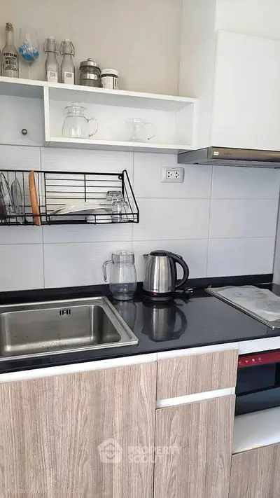 Modern kitchen with sleek cabinetry, stainless steel sink, and electric kettle on black countertop.
