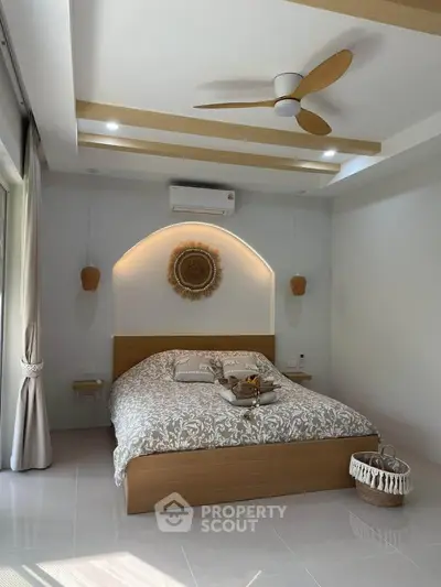 Modern bedroom with stylish decor, featuring a cozy bed, ceiling fan, and natural light from large windows.