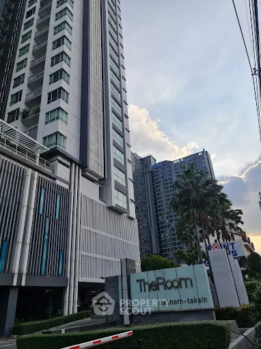 Modern high-rise building exterior with lush landscaping at The Room Sathorn-Taksin.