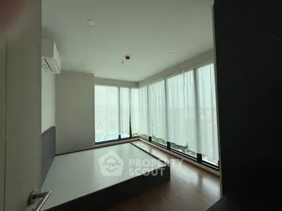 Spacious bedroom with large windows and modern design in a high-rise apartment.