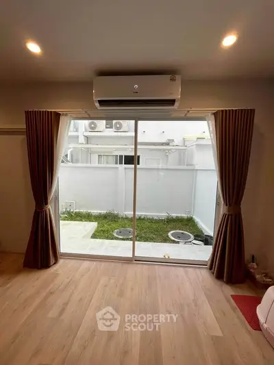 Spacious living room with large sliding glass doors opening to a private garden, featuring elegant curtains and modern air conditioning.