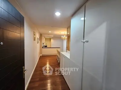 Spacious hallway leading to modern kitchen with wooden flooring and elegant lighting.
