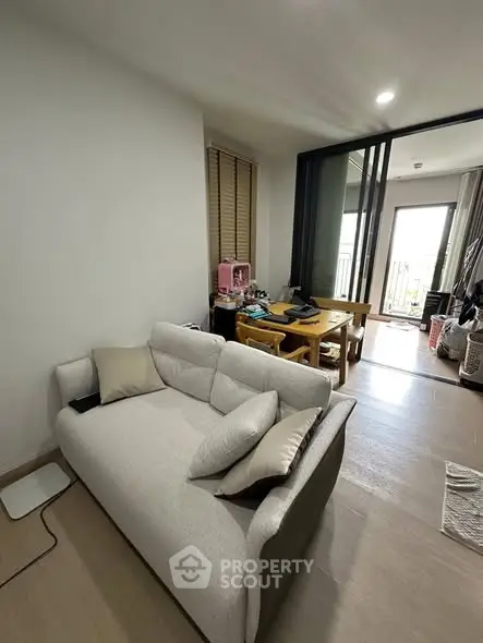 Cozy living room with modern sofa and dining area leading to a balcony, perfect for urban living.