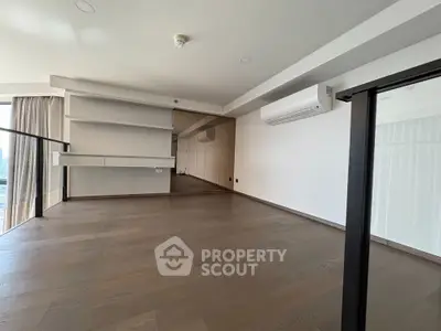 Spacious modern living room with hardwood floors and large windows offering city views.