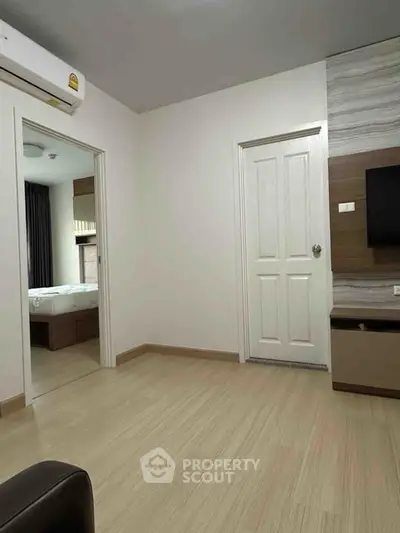 Modern apartment interior with wooden flooring, air conditioning, and a glimpse of a bedroom.