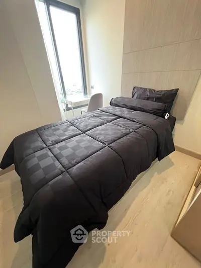 Modern bedroom with sleek black bedding and large window offering natural light.
