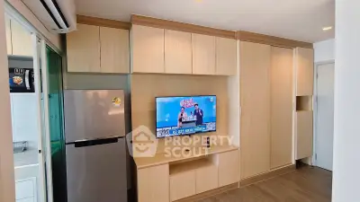 Modern apartment interior with built-in wooden cabinets and mounted TV, featuring a sleek refrigerator and air conditioning.