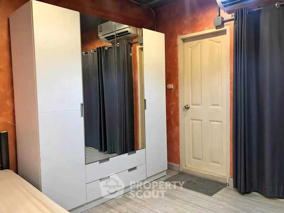 Cozy bedroom with modern wardrobe and air conditioning, featuring warm orange walls and sleek flooring.