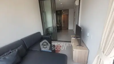 Modern living room with sleek black sofa and flat-screen TV, featuring sliding glass doors and neutral decor.