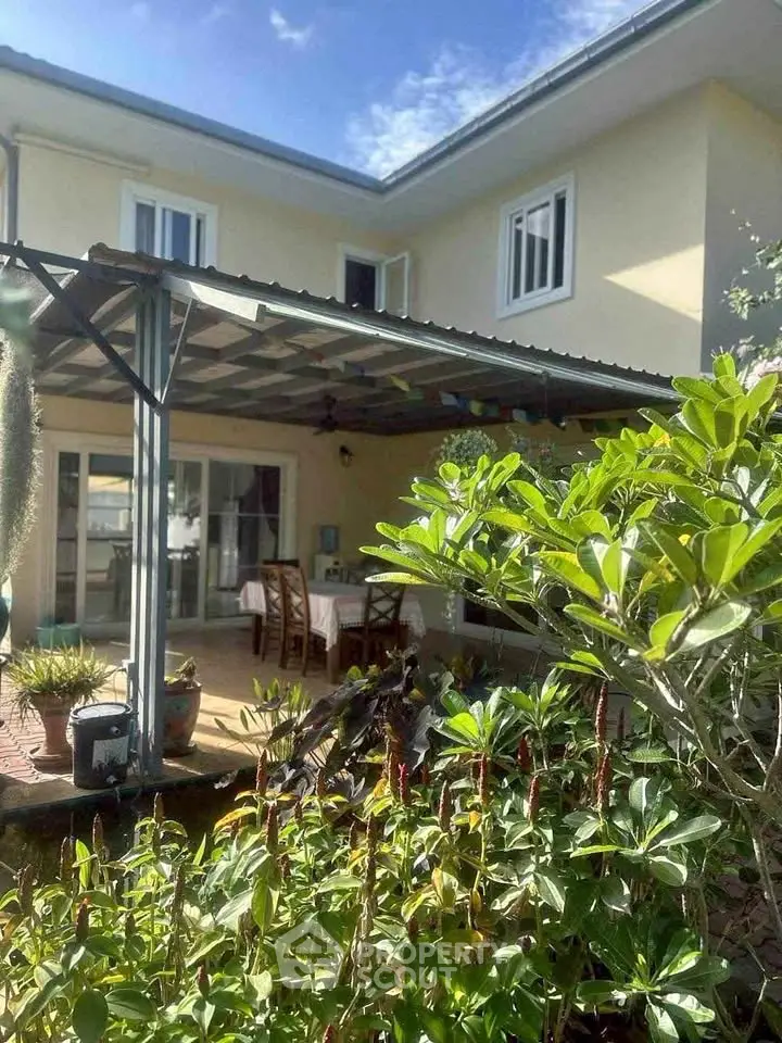 Charming two-story house with covered patio and lush garden, perfect for outdoor dining and relaxation.