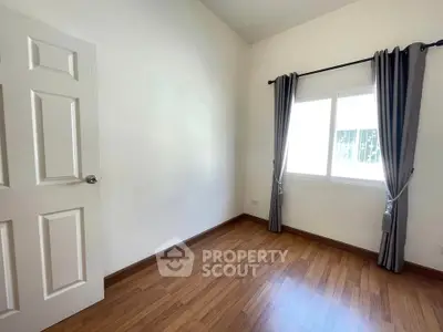 Bright empty room with wooden flooring and large window, perfect for customization.