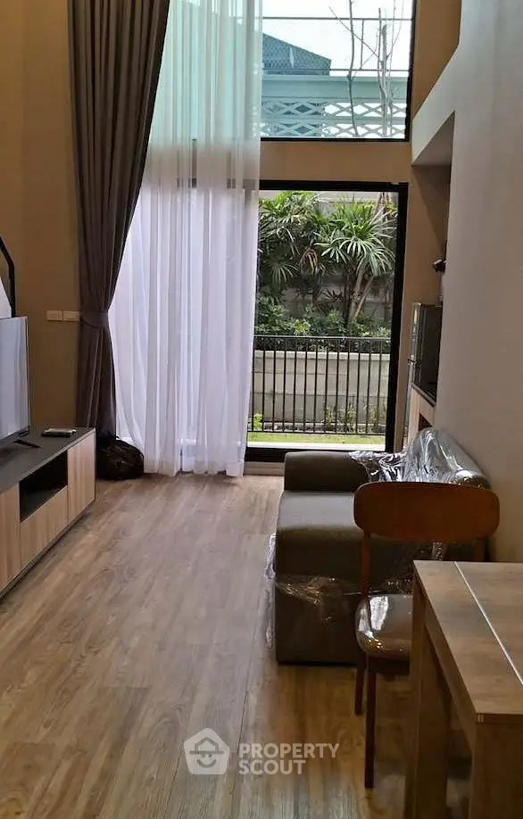 Modern living room with high ceilings and large windows overlooking a garden, featuring stylish furniture and wooden flooring.