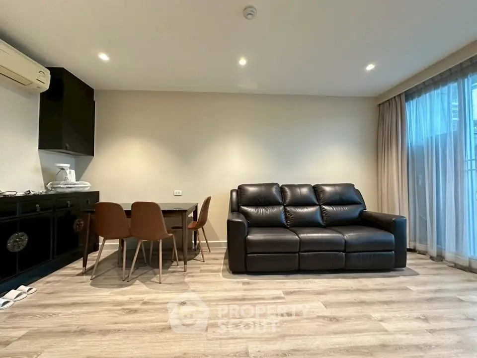 Modern living room with sleek black leather sofa and dining area, featuring elegant wood flooring and natural light.