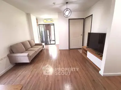 Spacious living room with modern decor and wooden flooring, featuring a comfortable sofa and large TV.