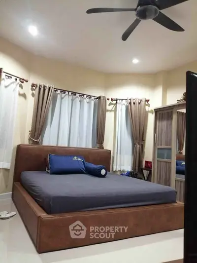 Spacious bedroom with modern furnishings and ceiling fan, featuring large windows and elegant curtains.