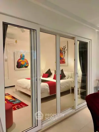Modern bedroom with glass sliding doors and vibrant artwork, featuring a cozy bed and stylish decor.